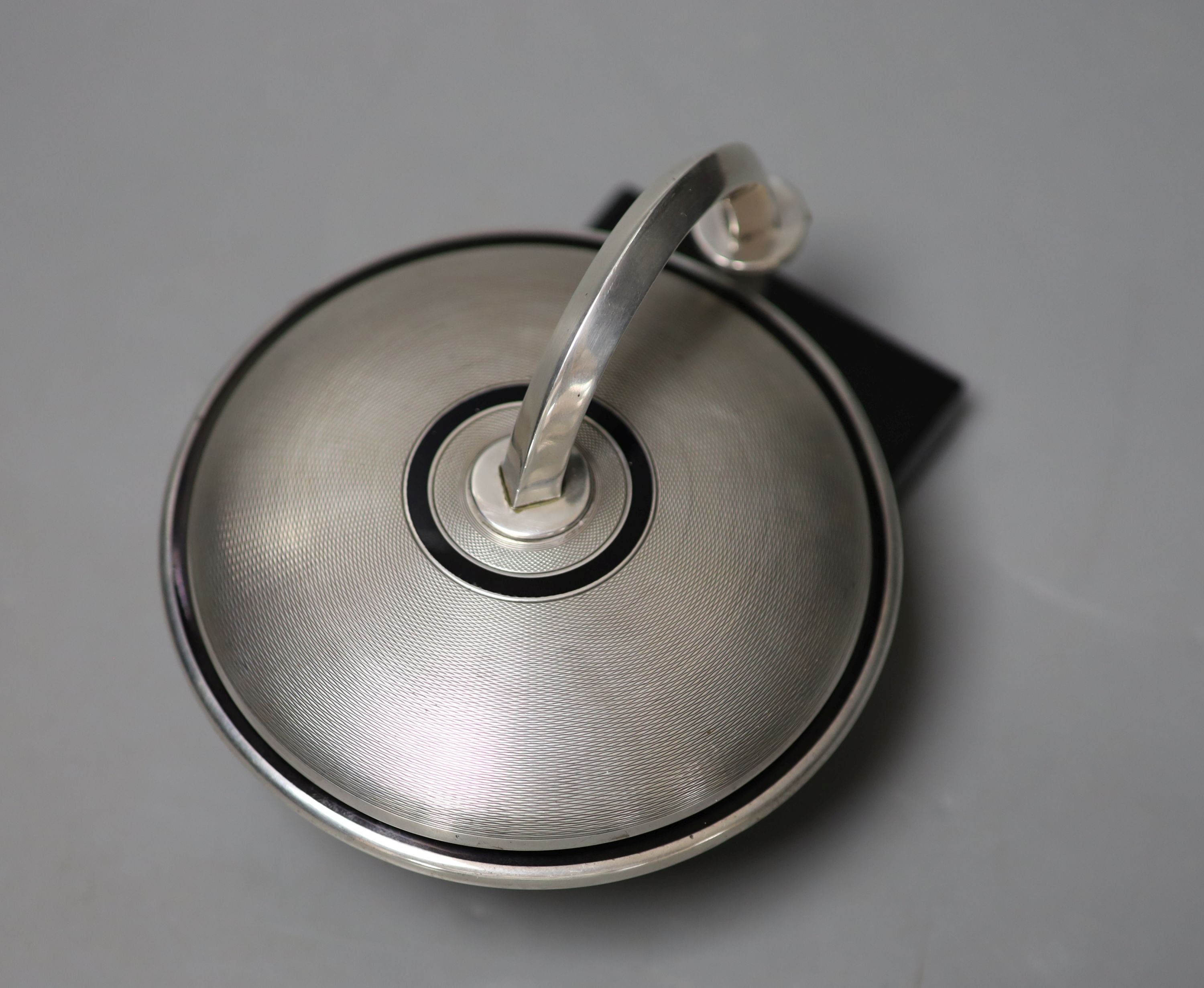 An unusual Art Deco engine turned silver and black enamel circular compact, with support arm, on black onyx? base (a.f.), Cohen & Charles, circa 1930, height 9.5cm.